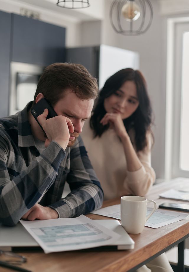 Un couple préoccupé, au téléphone avec des documents financiers sur la table